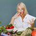 A surprised woman looking at a tablet surrounded by fresh vegetables and fruits, promoting healthy eating.