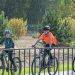 Three children riding bicycles on a sunny day along a park pathway, surrounded by greenery.